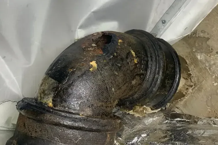 Corroded cast iron drain pipe leaking along its joints inside a building