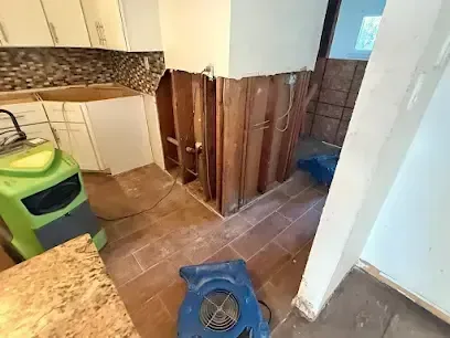 Kitchen with lower cabinets and walls opened and air movers drying after an appliance leak