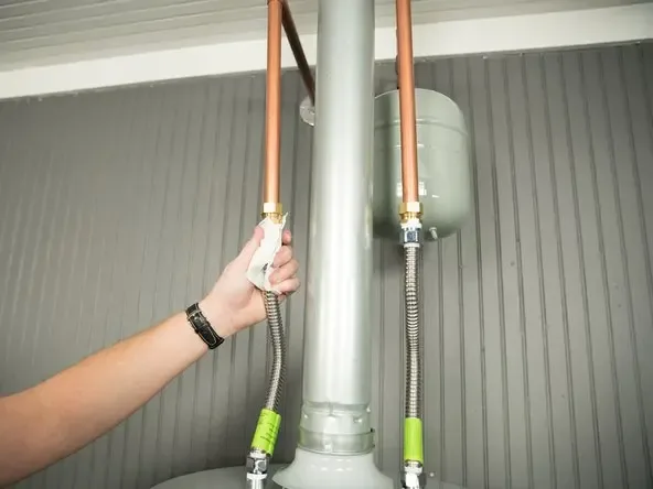 A hand checking the supply hose connections on top of a water heater for a leak